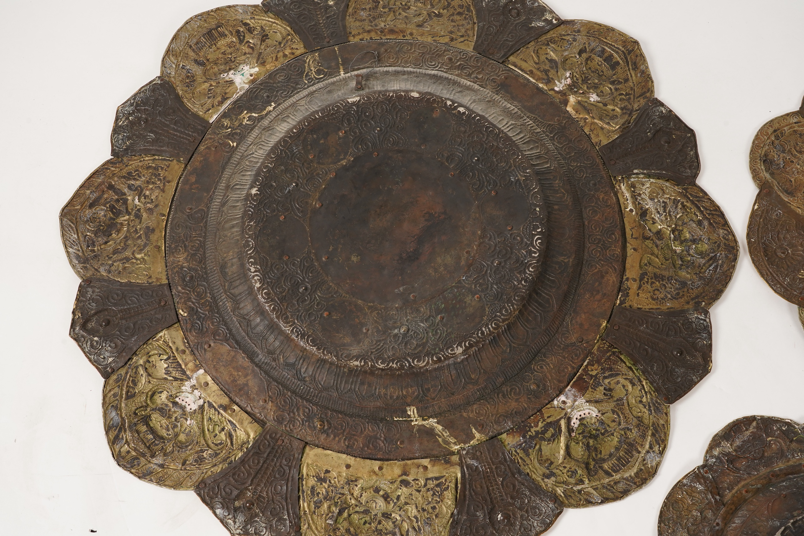 A graduated set of three Nepalese repoussé white metal and brass chargers, first half 20th century